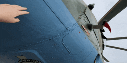 a person 's hand is touching the side of a blue airplane with a red flag on it