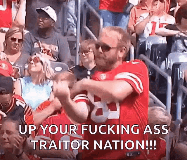 a man in a red jersey is dancing in the stands at a football game while a crowd watches .