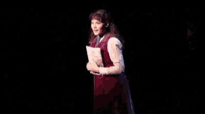 a young woman is singing into a microphone on a stage in a dark room .