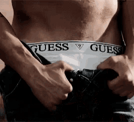 a man wearing guess underwear is taking off his pants .