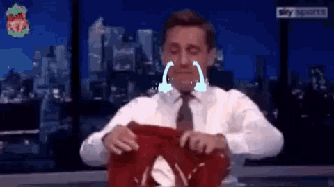 a man is crying while holding a liverpool shirt