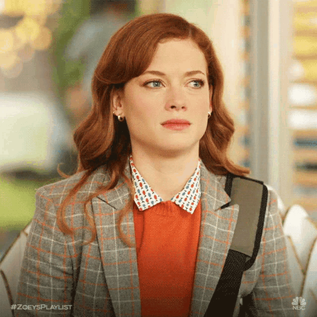 a woman with red hair is wearing a plaid jacket and orange sweater