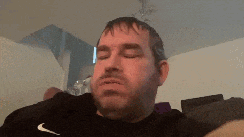 a man is sitting on a couch with his eyes closed and a nike shirt on .