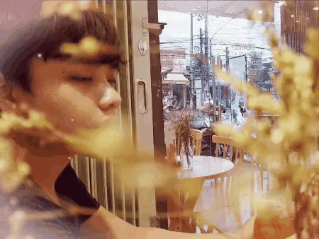 a man is looking out of a window at a table with a vase of flowers on it