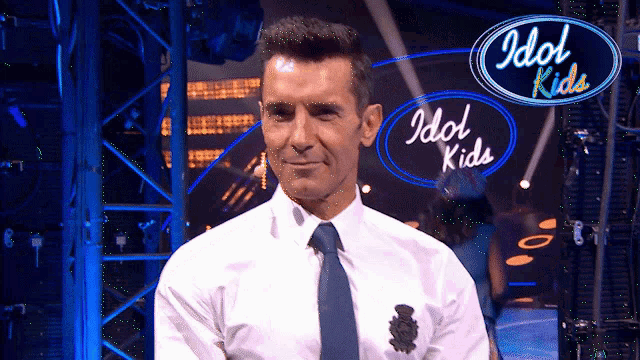 a man in a white shirt and tie is standing in front of a sign that says idol kids