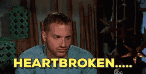 a man with a beard is sitting in front of a sign that says " heartbroken "