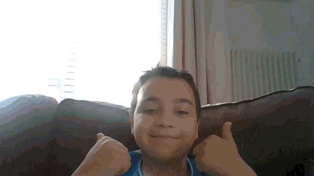 a young boy is sitting on a couch and giving a thumbs up