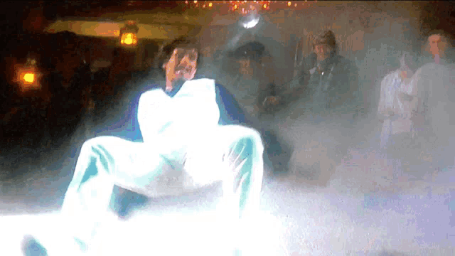 a man in a white and blue shirt is dancing in a dark room