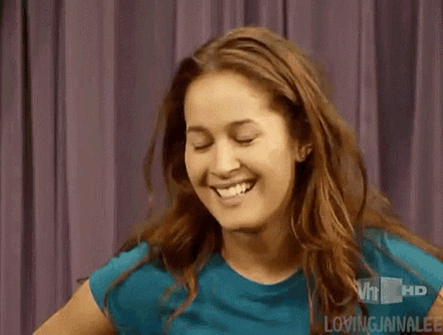 a woman in a blue shirt is smiling in front of a purple curtain on vh1 hd .