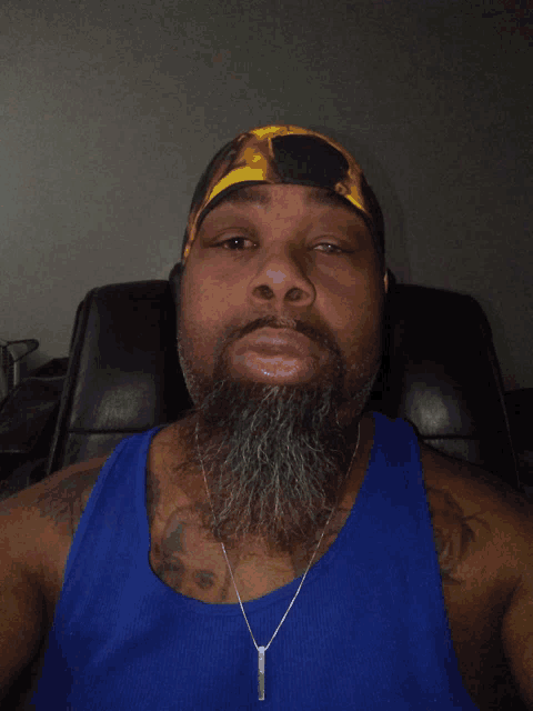 a man with a beard is wearing a blue tank top and a necklace