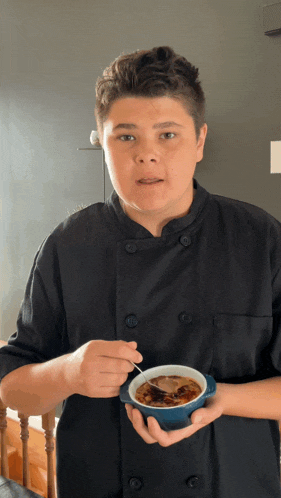 a young man in a chef 's uniform is holding a bowl of food with a spoon