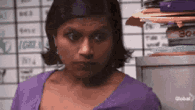 a woman in a purple shirt is standing in front of a stack of paperwork .