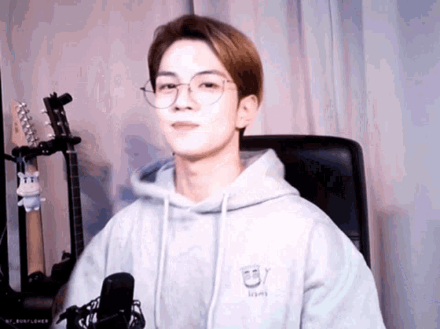 a young man wearing glasses and a hoodie is sitting in a chair in front of a microphone .
