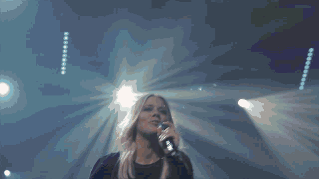 a woman singing into a microphone in front of a crowd with their hands in the air