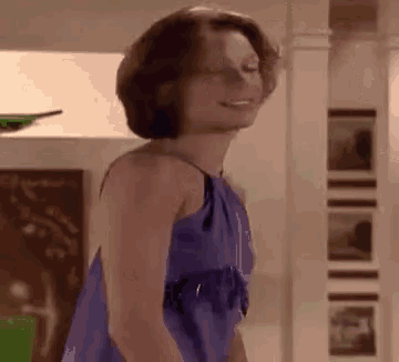 a woman in a purple dress is smiling and dancing in a living room .