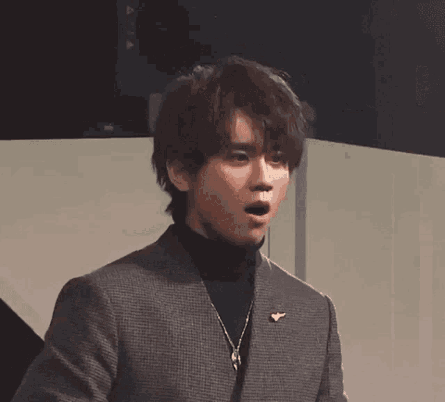 a young man wearing a suit and a black turtleneck is standing in front of a wall .