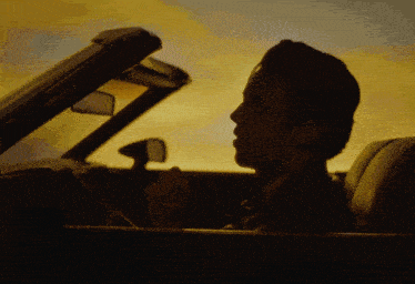 a man in a convertible car looks out the window at the sunset