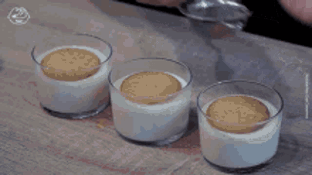 a person is pouring powdered sugar into three cups of dessert with cookies on top .