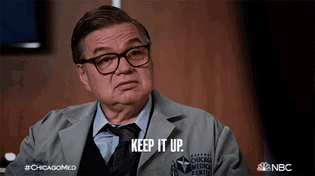 a man wearing glasses and a lab coat says " keep it up "