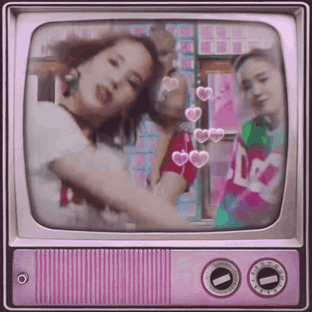 three women are dancing in front of a pink tv with hearts on it