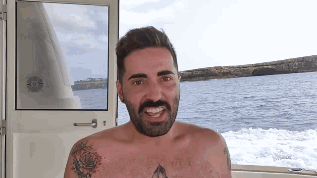 a shirtless man with a tattoo on his chest stands in front of a window overlooking the water
