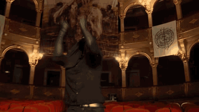 a man in a black hoodie is standing in an auditorium with red seats