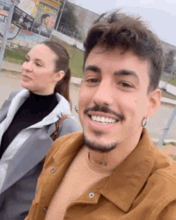 a man and a woman are standing next to each other and smiling . the man has a tattoo on his neck .