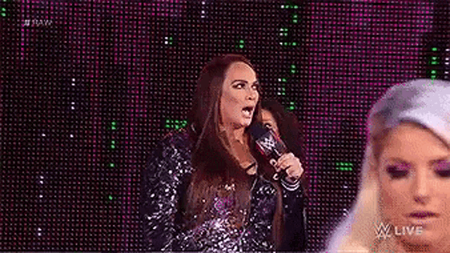 a woman is speaking into a microphone on a stage while another woman looks on .
