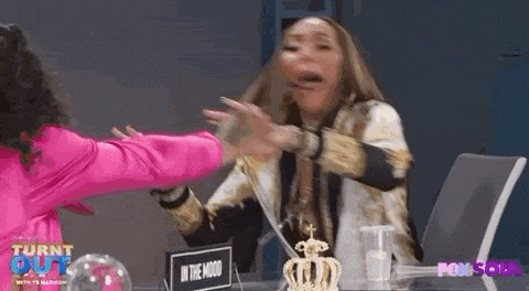 two women are sitting at a table having a fight . one of the women is wearing a pink jacket .