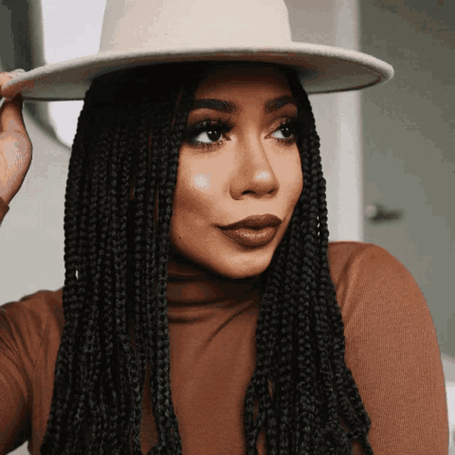 a woman with braids wearing a hat and brown turtleneck