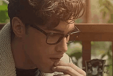 a man wearing glasses and a scarf is eating a sandwich .