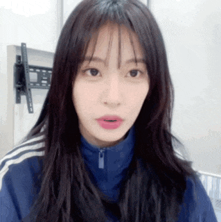 a woman with long hair and bangs is wearing a blue jacket and looking at the camera .
