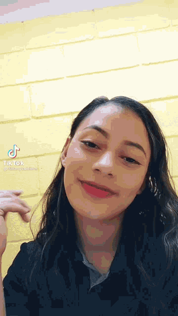 a woman 's face is shown in front of a yellow brick wall with tik tok written on the bottom