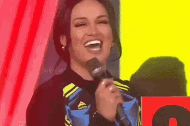 a woman is laughing while holding a microphone in front of a yellow background .