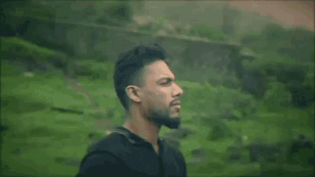 a man with a beard is standing in a field looking at the camera .