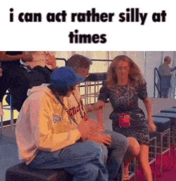a man is sitting on a stool next to a woman on a red carpet while a woman is dancing .