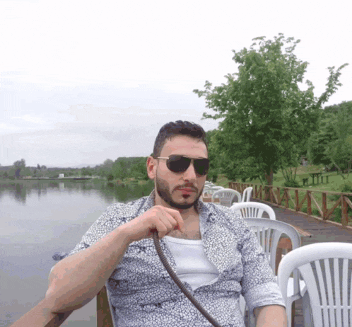 a man wearing sunglasses sits in a chair near a lake