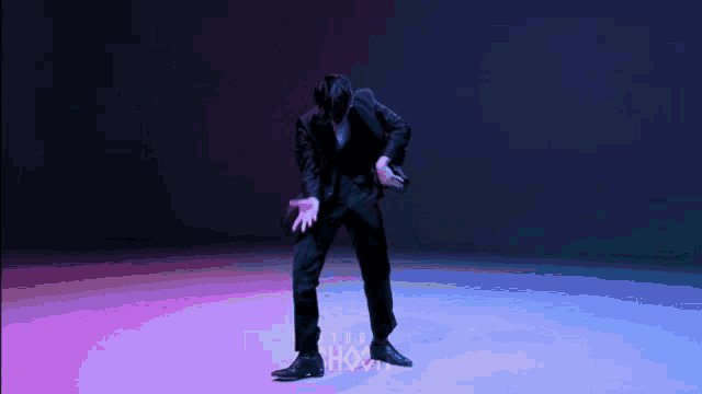a man in a black suit is dancing in front of a purple and blue background that says show