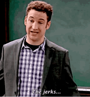 a man in a suit says " the jerks " in front of a blackboard