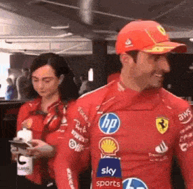 a man and a woman are standing next to each other wearing red ferrari shirts .