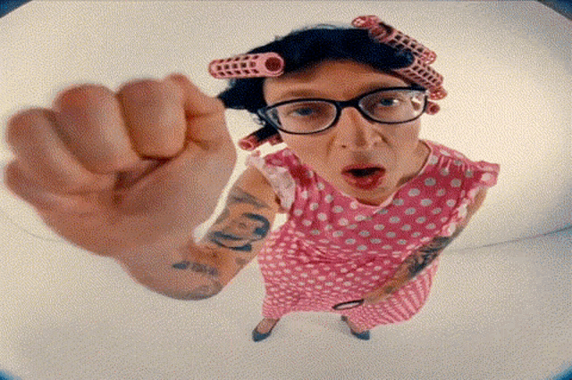 a woman in a pink polka dot dress with curlers on her head is giving a fist bump .