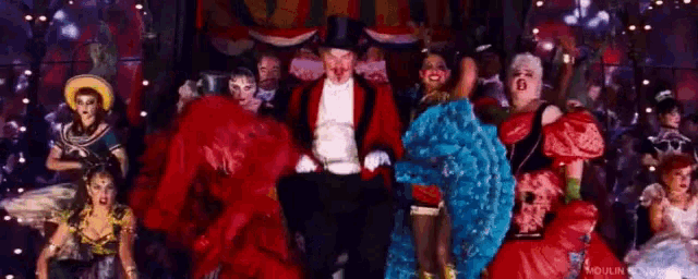 a man in a top hat is surrounded by a group of women in colorful costumes