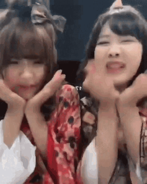 two young women are making funny faces with their hands over their faces .