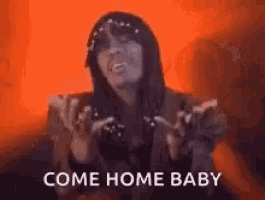 a woman is sitting on a couch with her hands outstretched and the words `` come home baby '' written on her face .