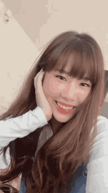 a woman with long brown hair and bangs is smiling and touching her face