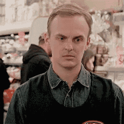a man wearing a black apron is standing in a grocery store .