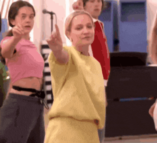 a woman in a yellow shirt is dancing in front of a microphone while a group of people watch .
