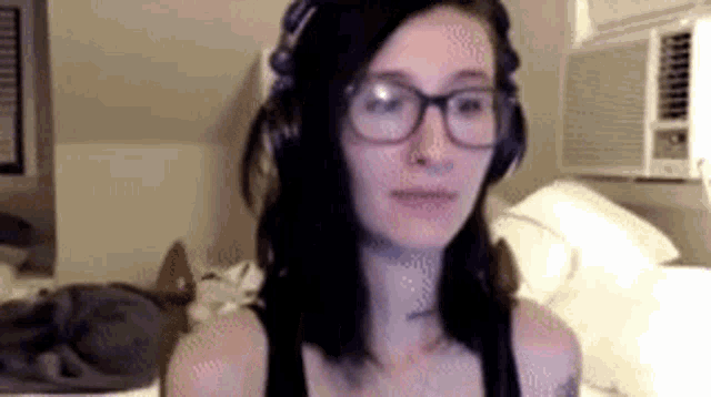a woman wearing glasses and headphones is sitting on a bed in a room .
