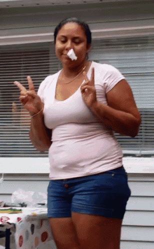 a woman in a pink shirt and blue shorts is holding a piece of paper in her mouth