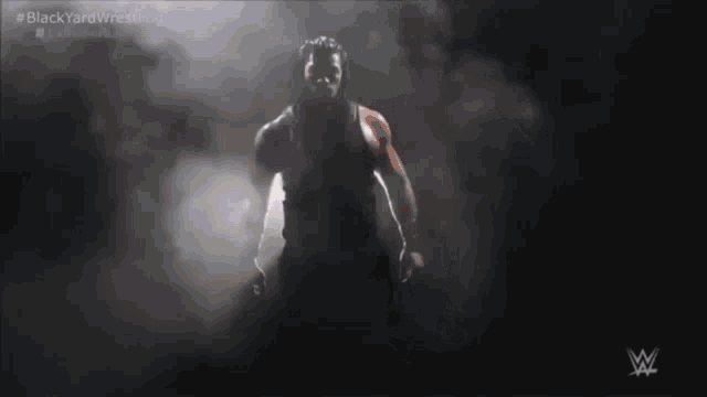 a wrestler is standing in a dark room with smoke coming out of his mouth